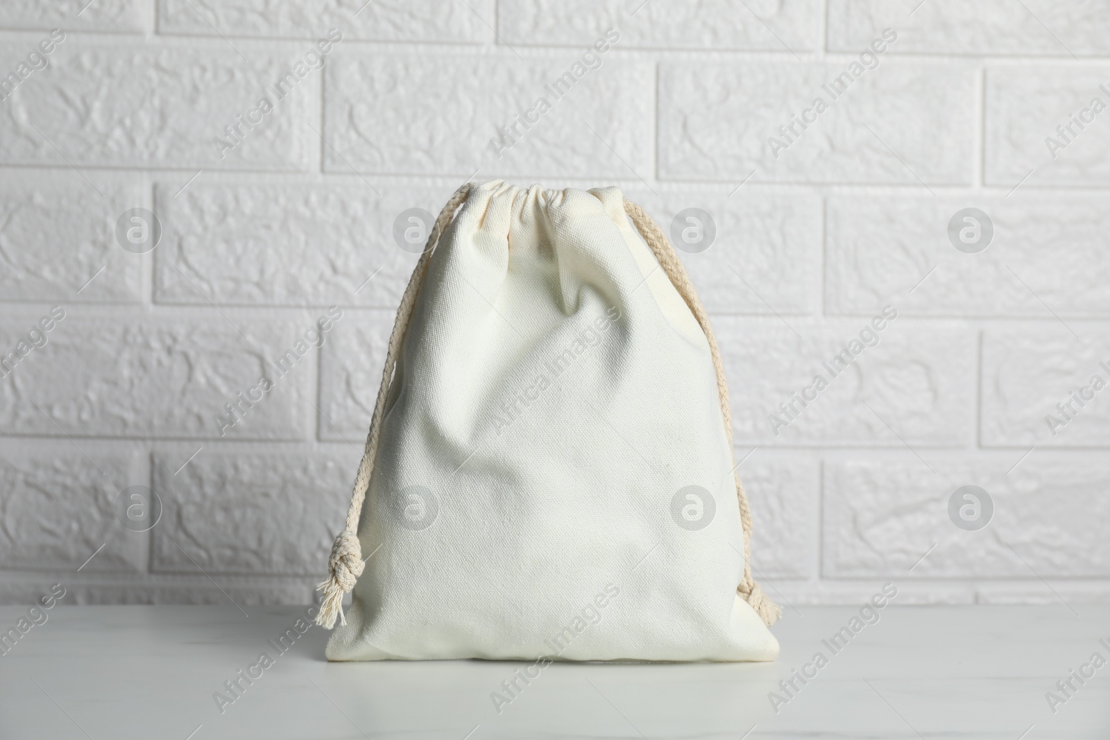 Photo of One cotton bag on marble table against white brick wall