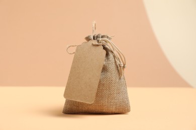 Photo of One burlap bag with tag on table against beige background