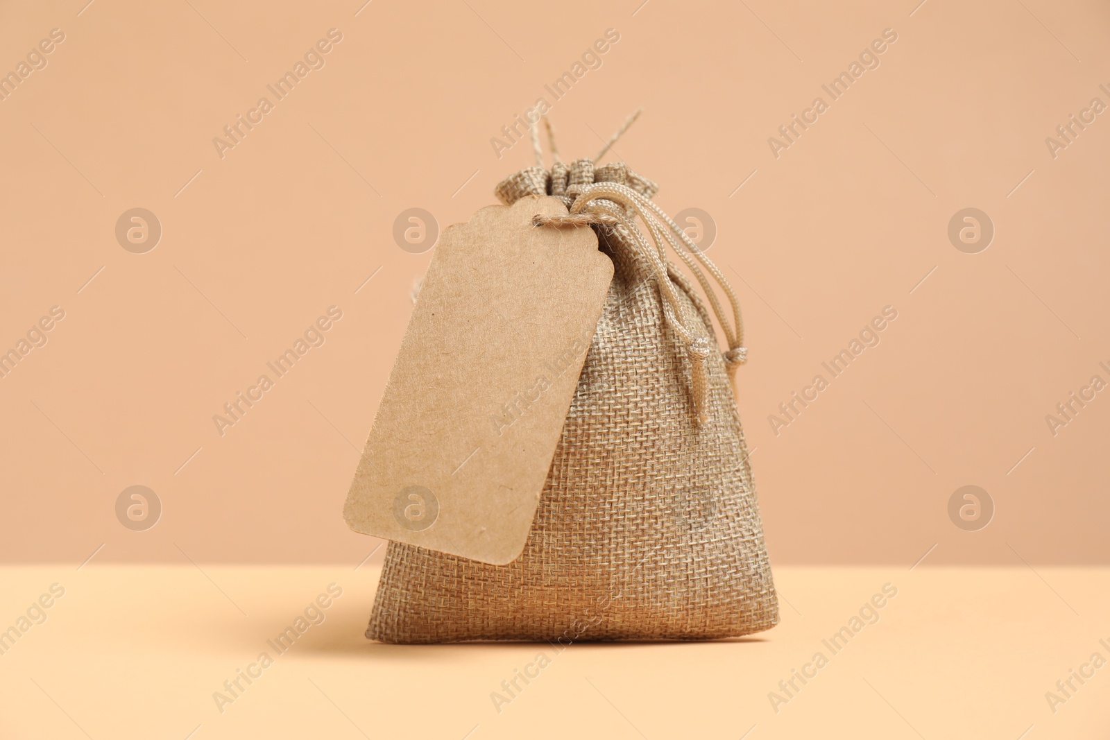 Photo of One burlap bag with tag on table against beige background