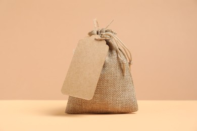 One burlap bag with tag on table against beige background