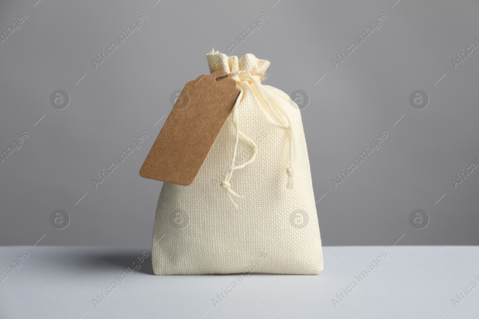 Photo of One burlap bag with tag on light table against grey background