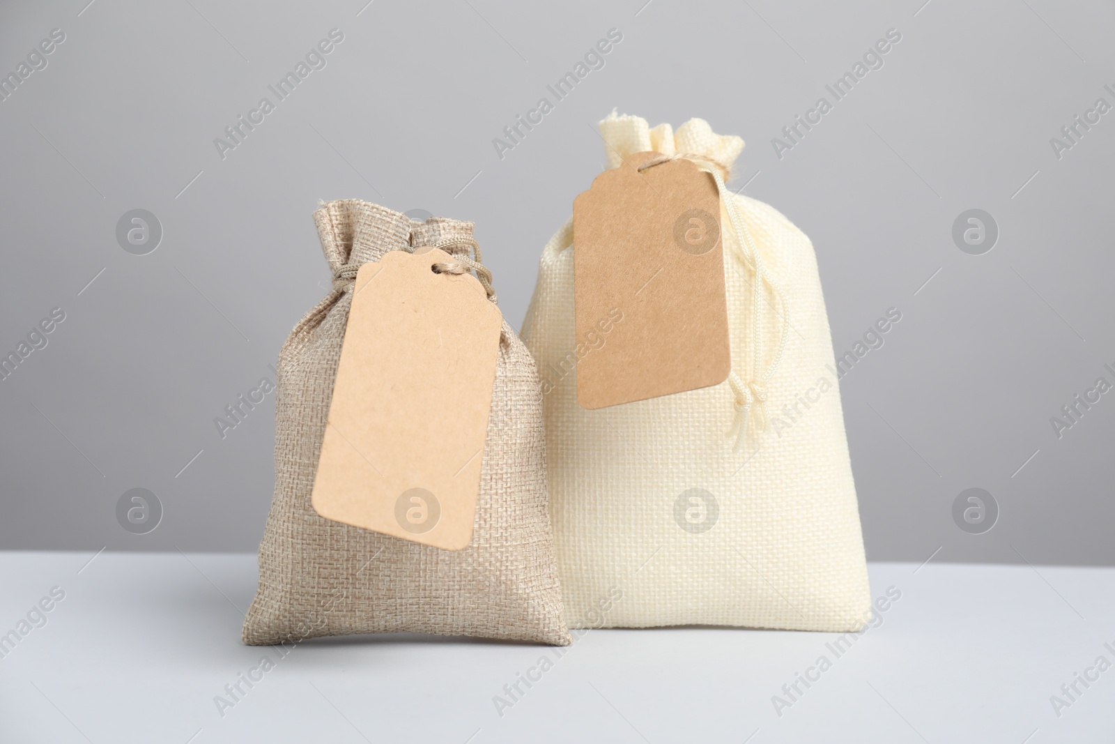 Photo of Burlap bags with tags on light table against grey background