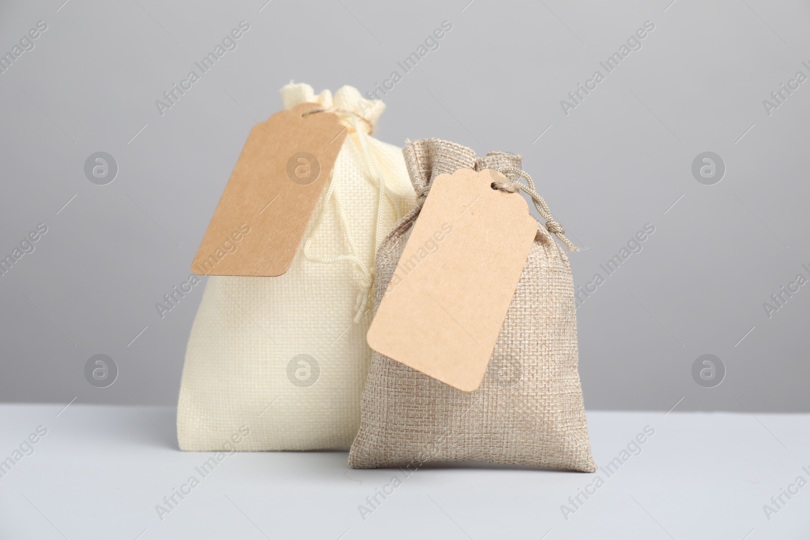 Photo of Burlap bags with tags on light table against grey background