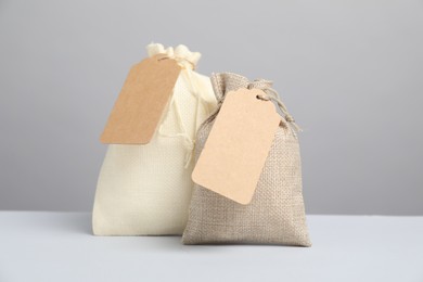 Photo of Burlap bags with tags on light table against grey background