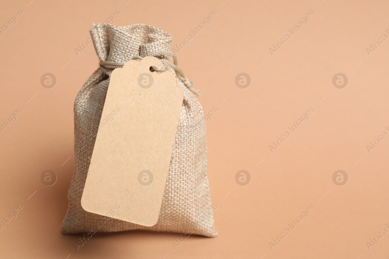 Photo of One burlap bag with tag on beige background, space for text