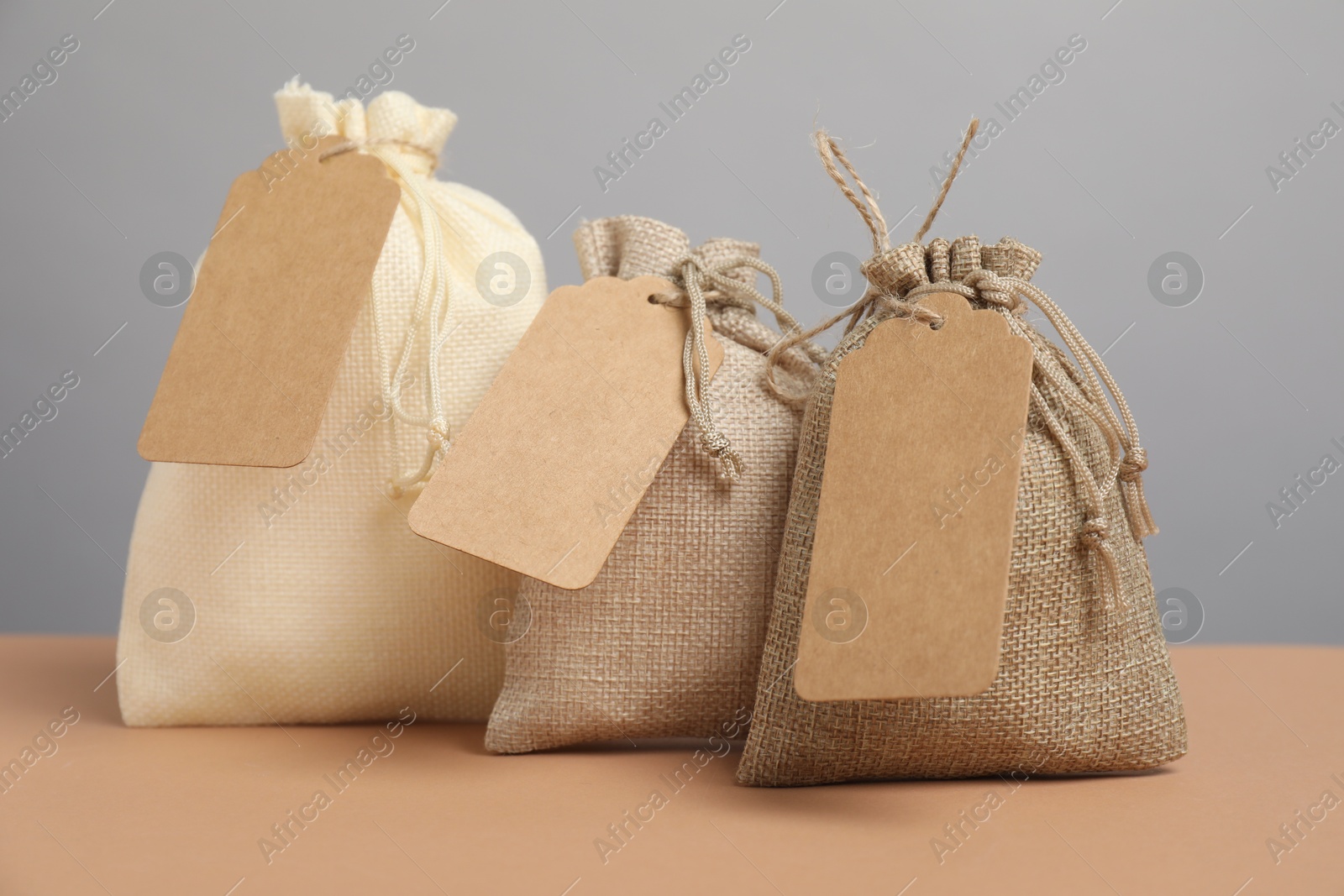 Photo of Burlap bags with tags on beige table against grey background