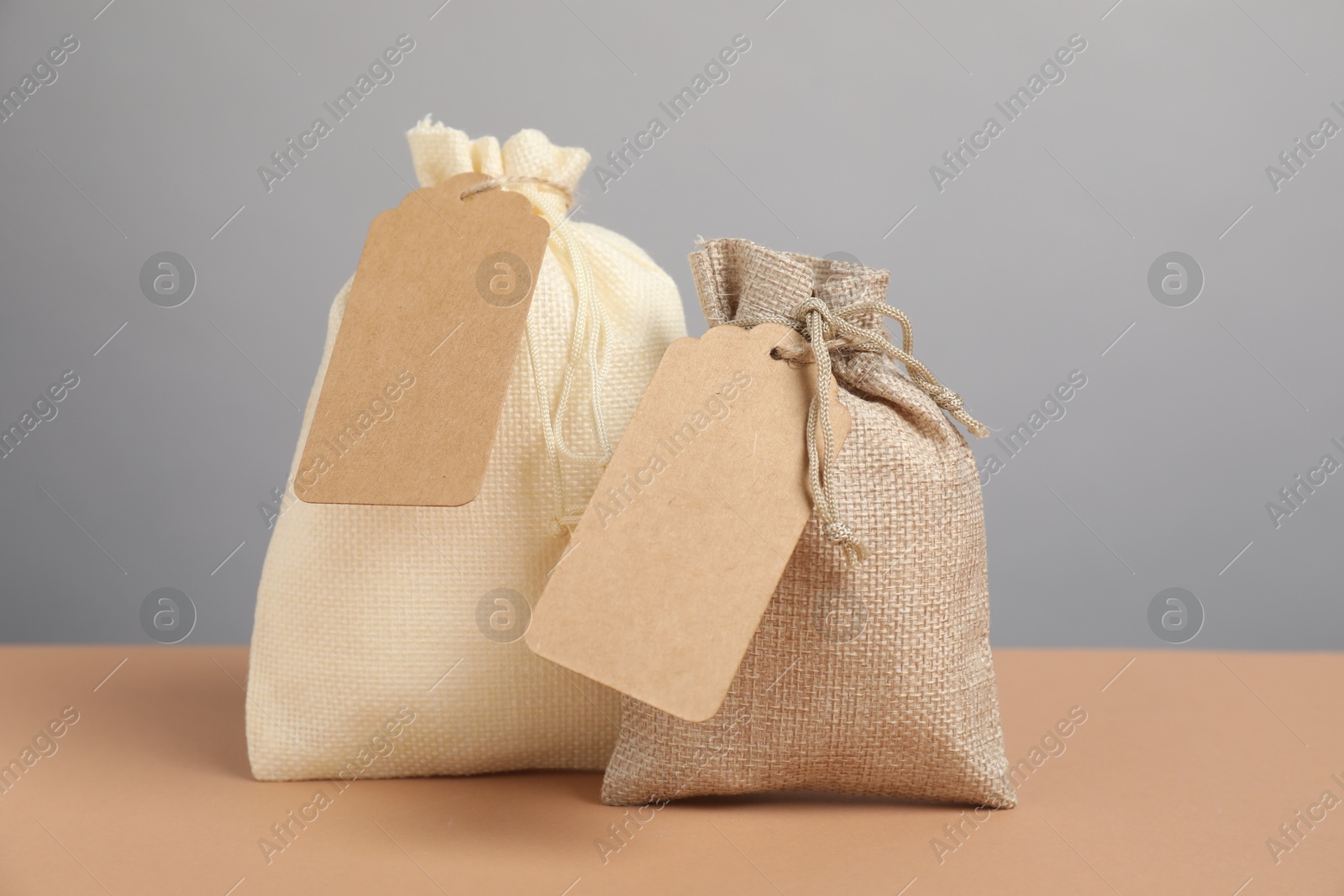 Photo of Burlap bags with tags on beige table against grey background