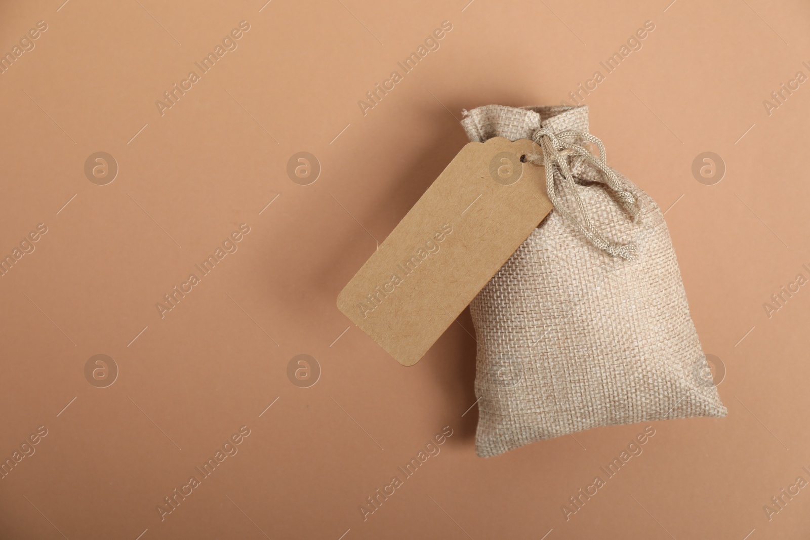 Photo of One burlap bag with tag on beige background, top view. Space for text