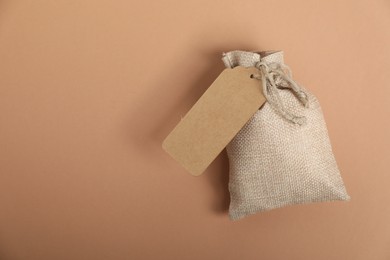 One burlap bag with tag on beige background, top view. Space for text