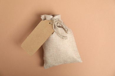 One burlap bag with tag on beige background, top view