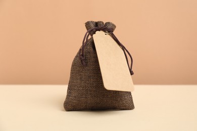 Burlap bag with tag on table against beige background