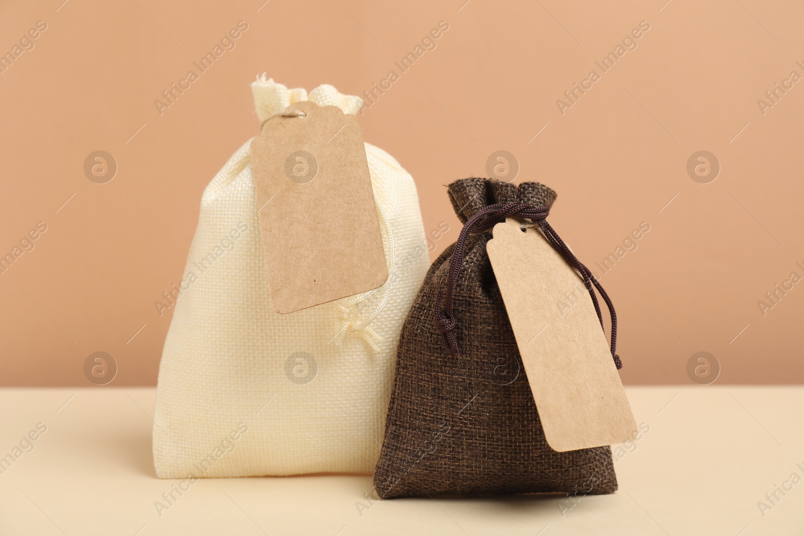 Photo of Burlap bags with tags on table against beige background