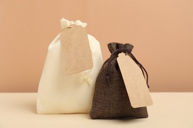 Burlap bags with tags on table against beige background