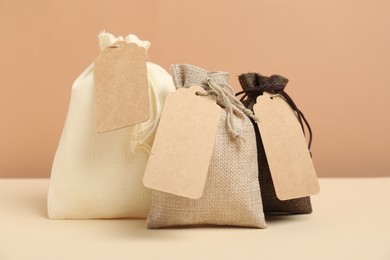 Burlap bags with tags on table against beige background