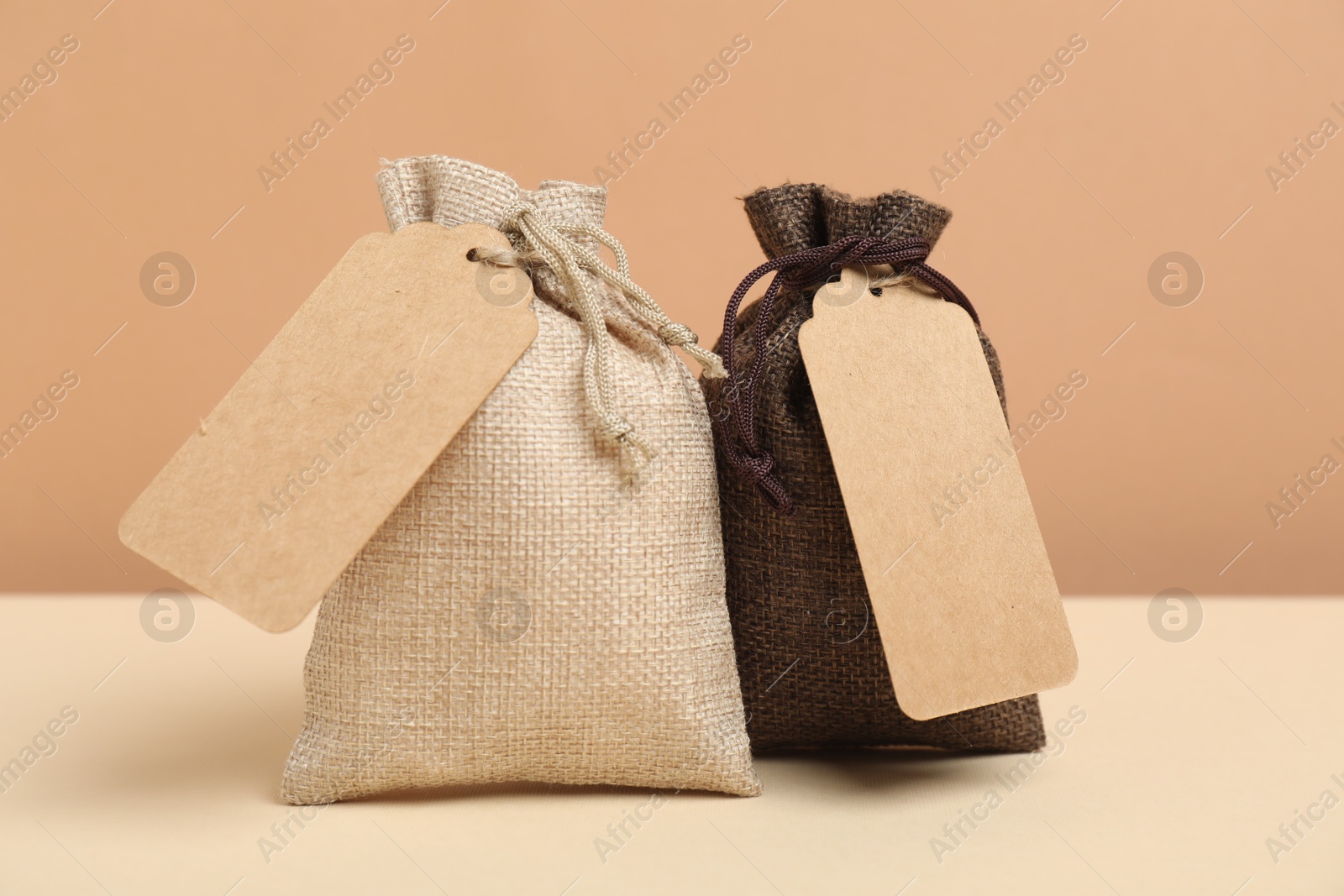 Photo of Burlap bags with tags on table against beige background