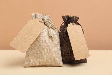 Photo of Burlap bags with tags on table against beige background