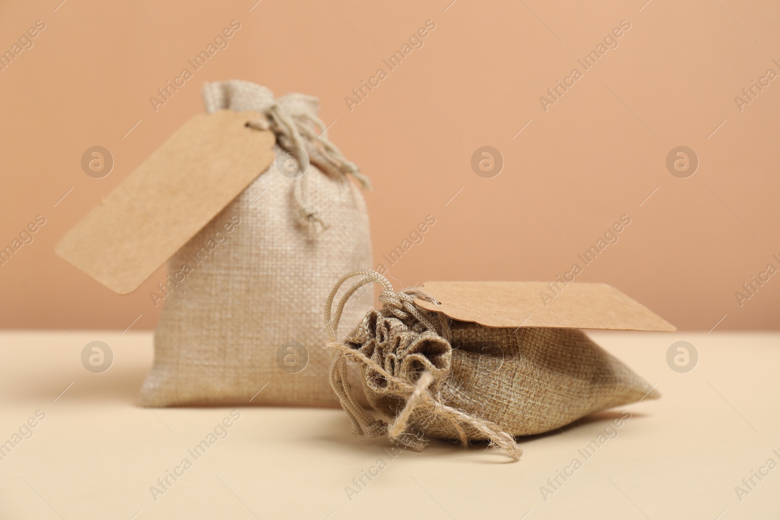 Photo of Burlap bags with tags on table against beige background