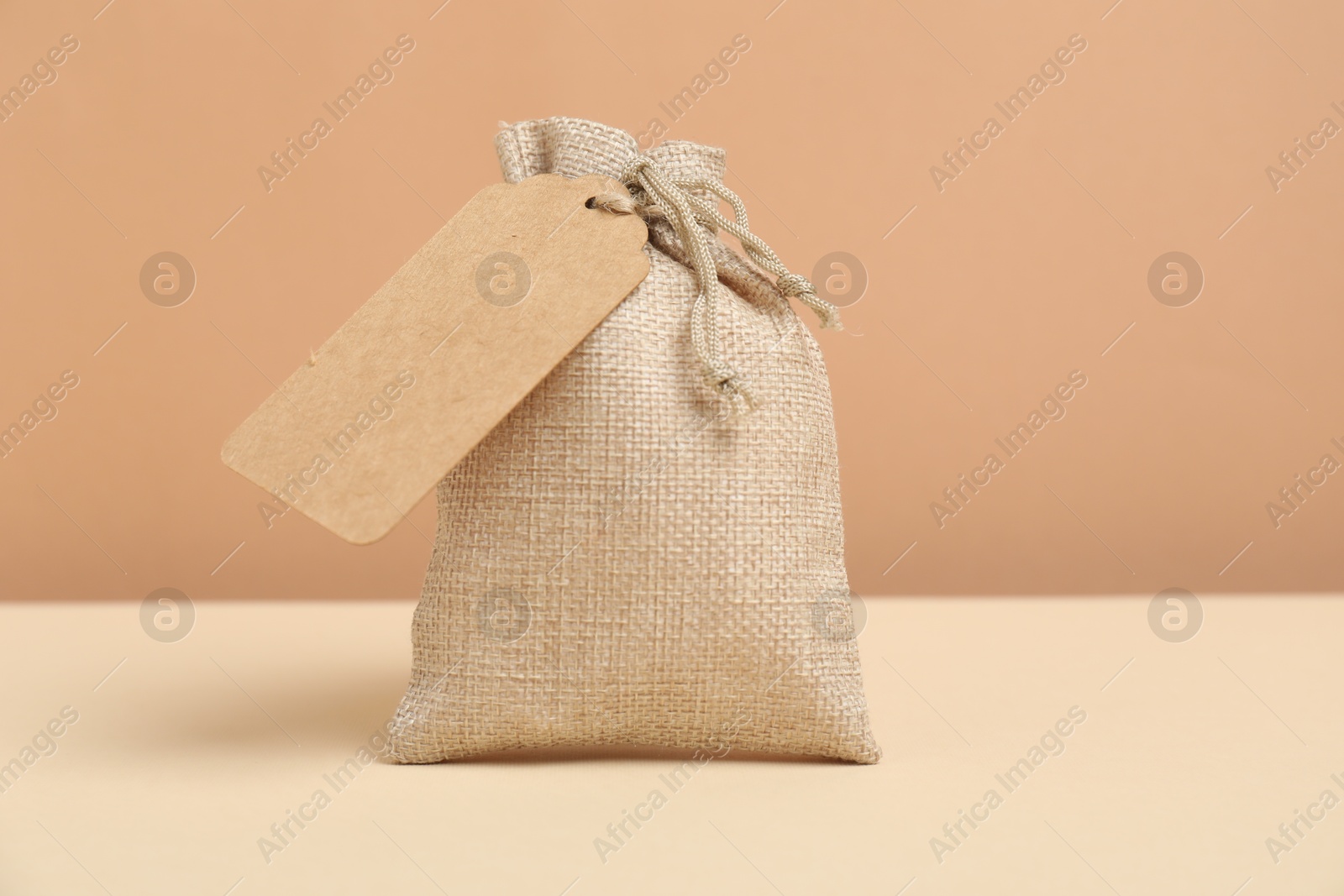 Photo of Burlap bag with tag on table against beige background