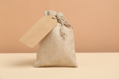 Burlap bag with tag on table against beige background