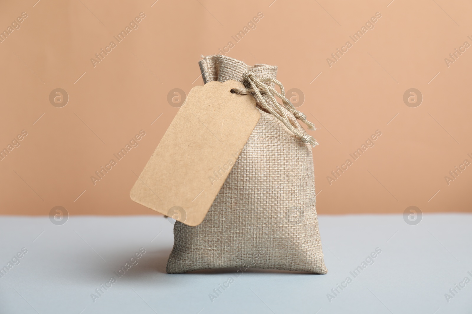 Photo of Burlap bag with tag on light grey table against beige background