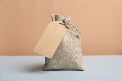 Burlap bag with tag on light grey table against beige background