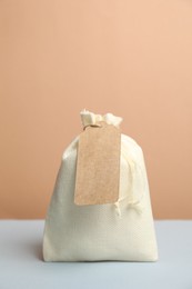 Photo of Burlap bag with tag on light grey table against beige background