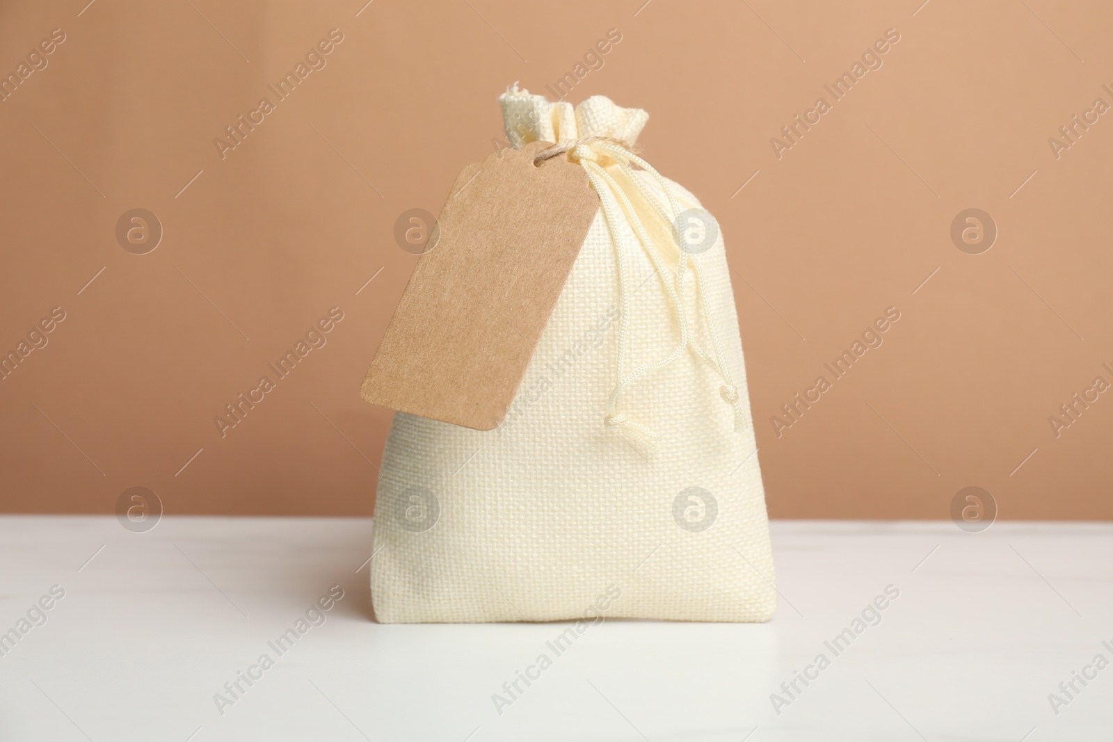 Photo of One burlap bag with tag on white table against dark beige background