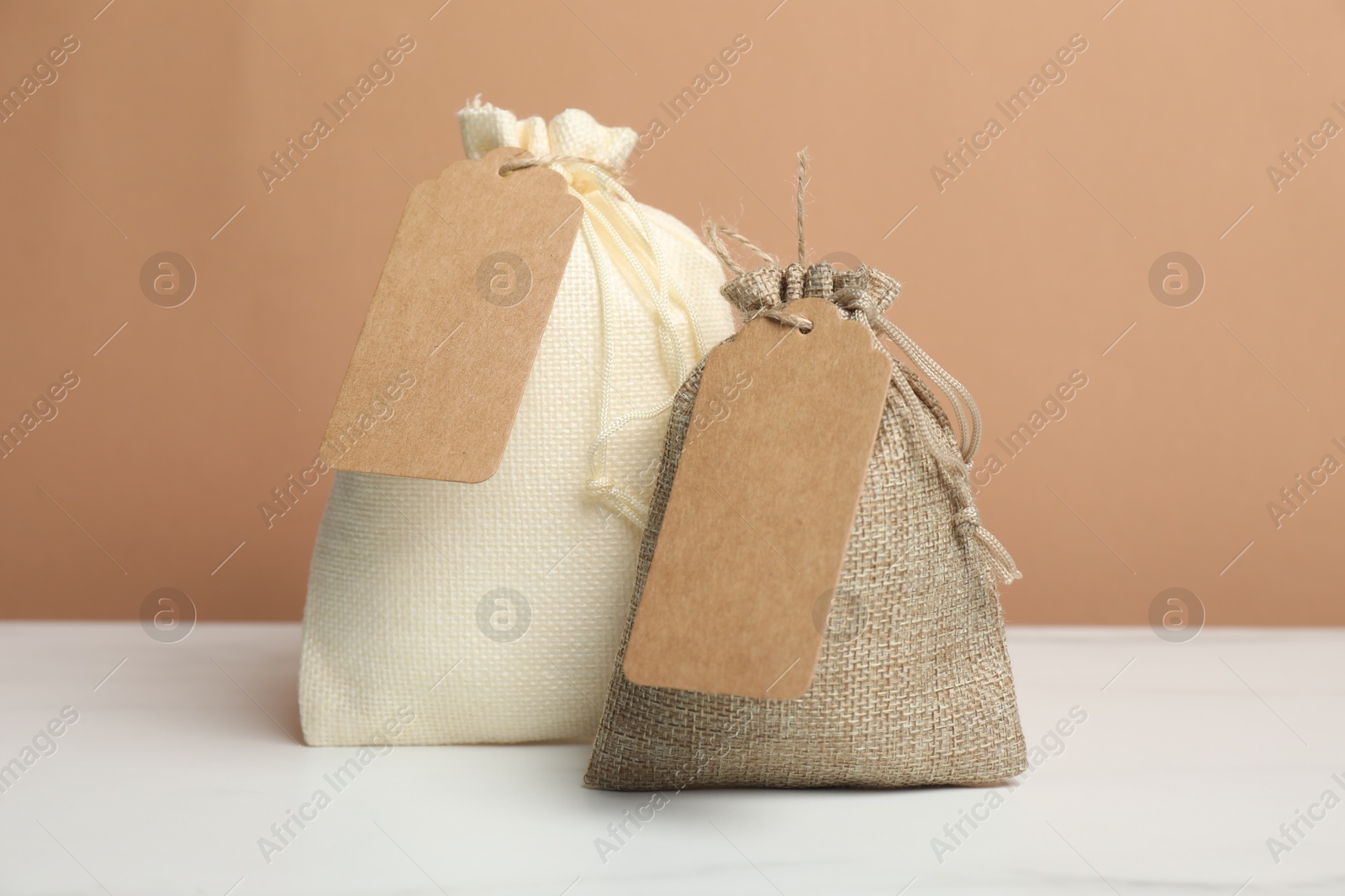 Photo of Burlap bags with tags on white table against dark beige background