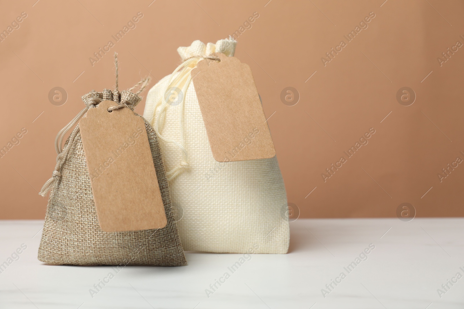 Photo of Burlap bags with tags on white marble table against dark beige background, space for text