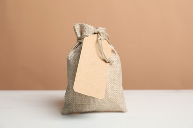 Photo of One burlap bag with tag on white table against dark beige background