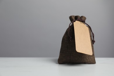 One burlap bag with tag on white marble table against grey background, space for text