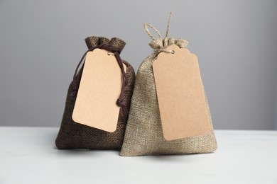 Burlap bags with tags on white table against grey background