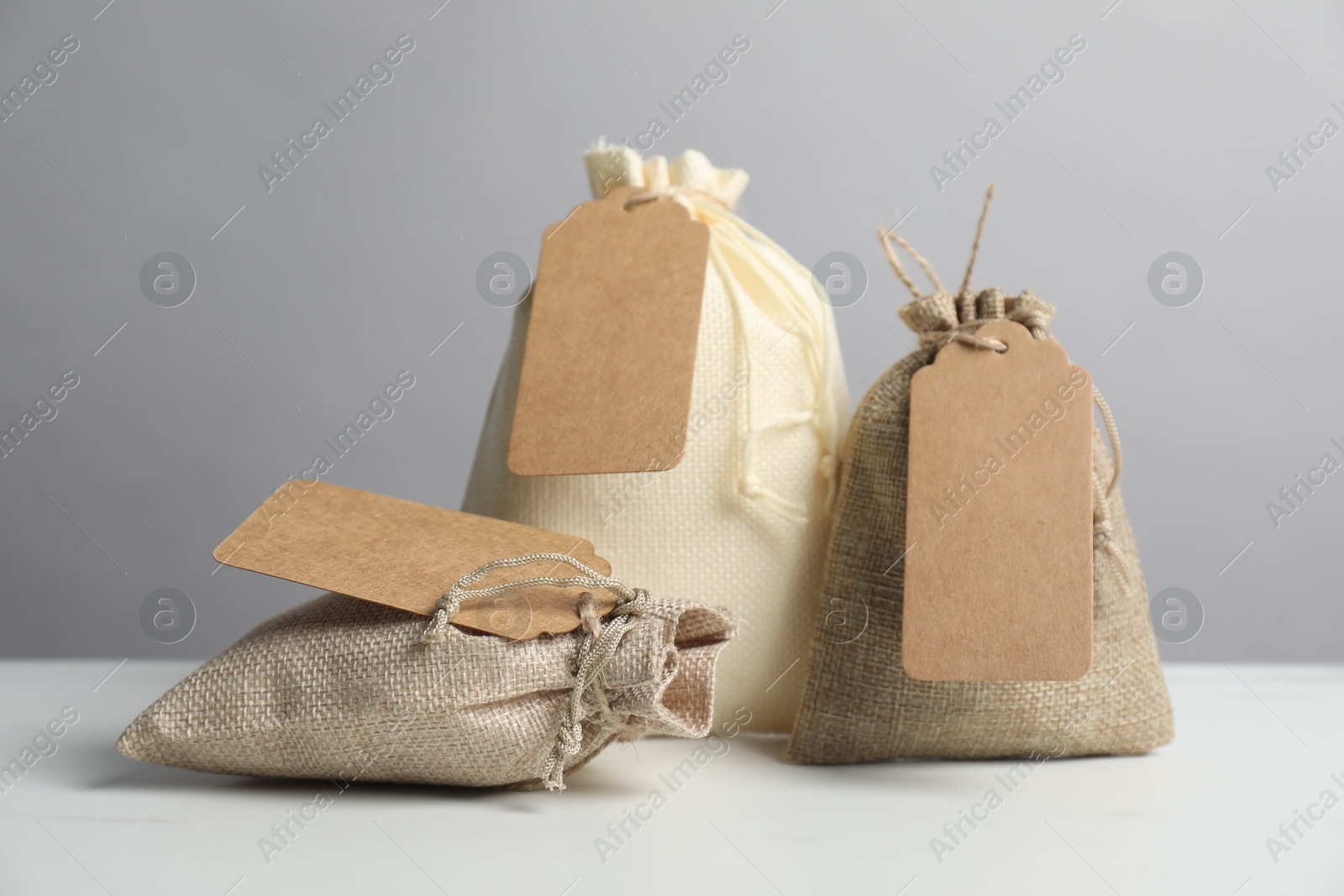 Photo of Burlap bags with tags on white table against grey background