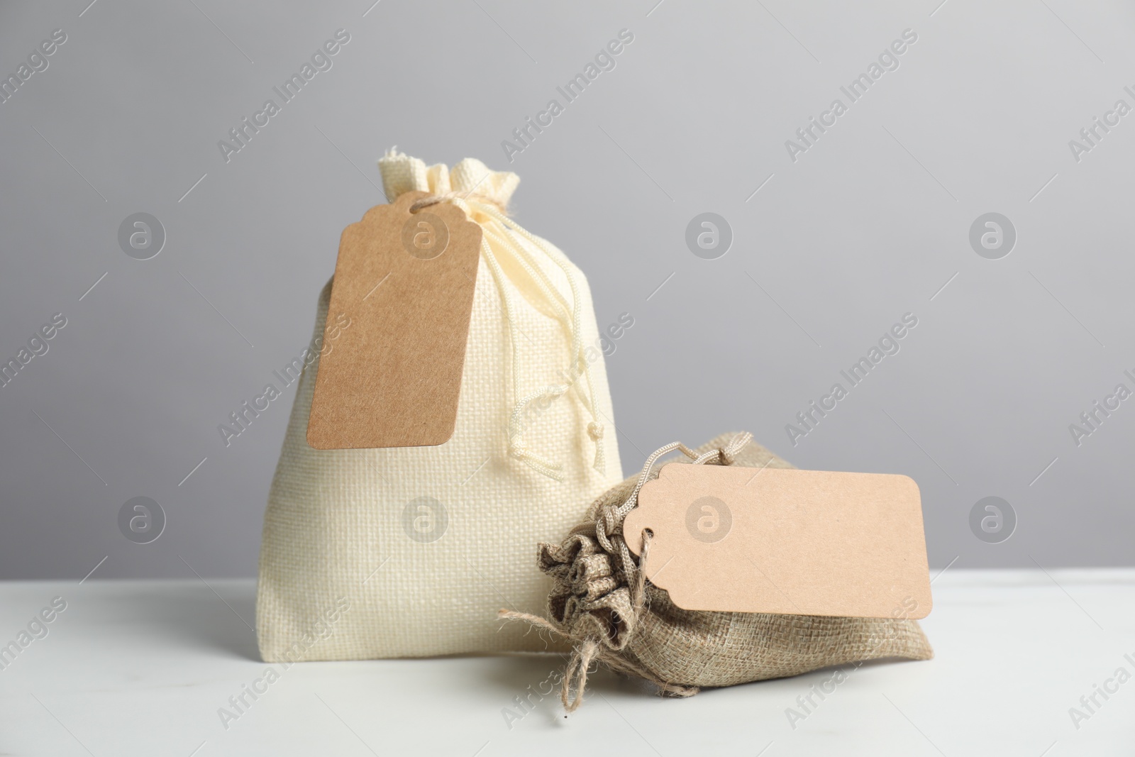 Photo of Burlap bags with tags on white table against grey background