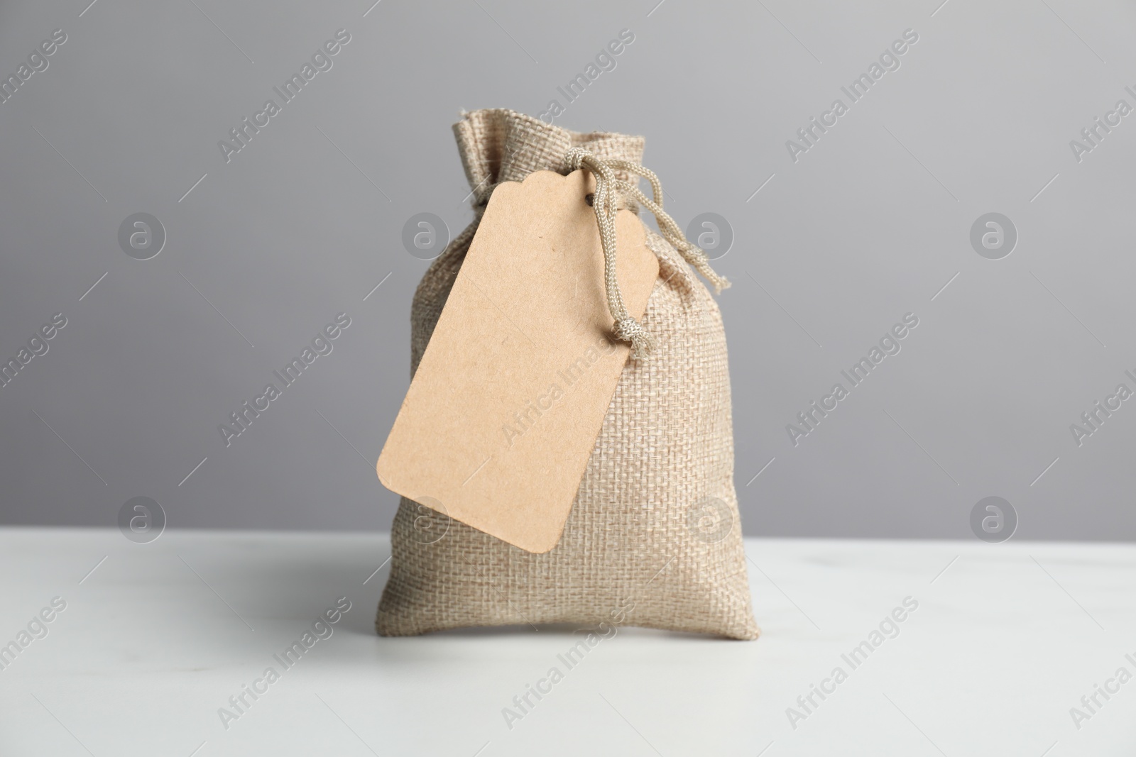 Photo of One burlap bag with tag on white table against grey background