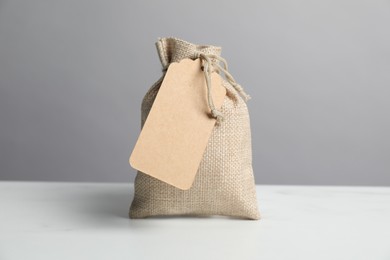 Photo of One burlap bag with tag on white table against grey background