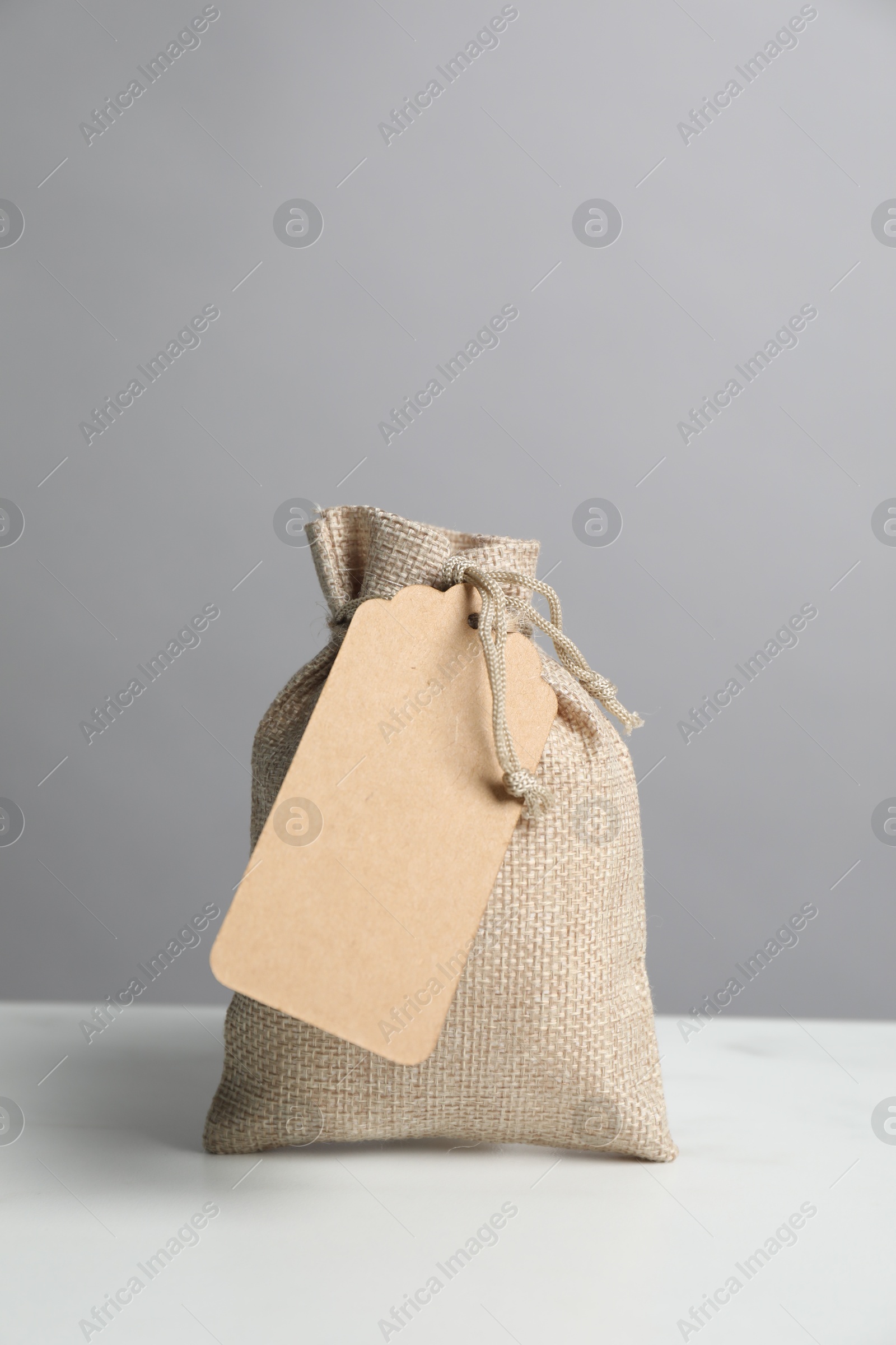 Photo of One burlap bag with tag on white table against grey background