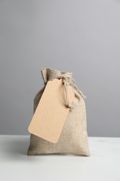 Photo of One burlap bag with tag on white table against grey background