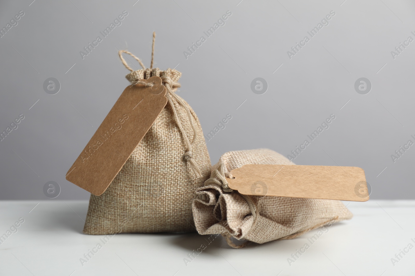 Photo of Burlap bags with tags on white table against grey background