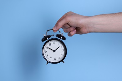 Photo of Man with black alarm clock on light blue background, closeup