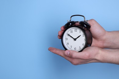 Photo of Man with black alarm clock on light blue background, closeup. Space for text