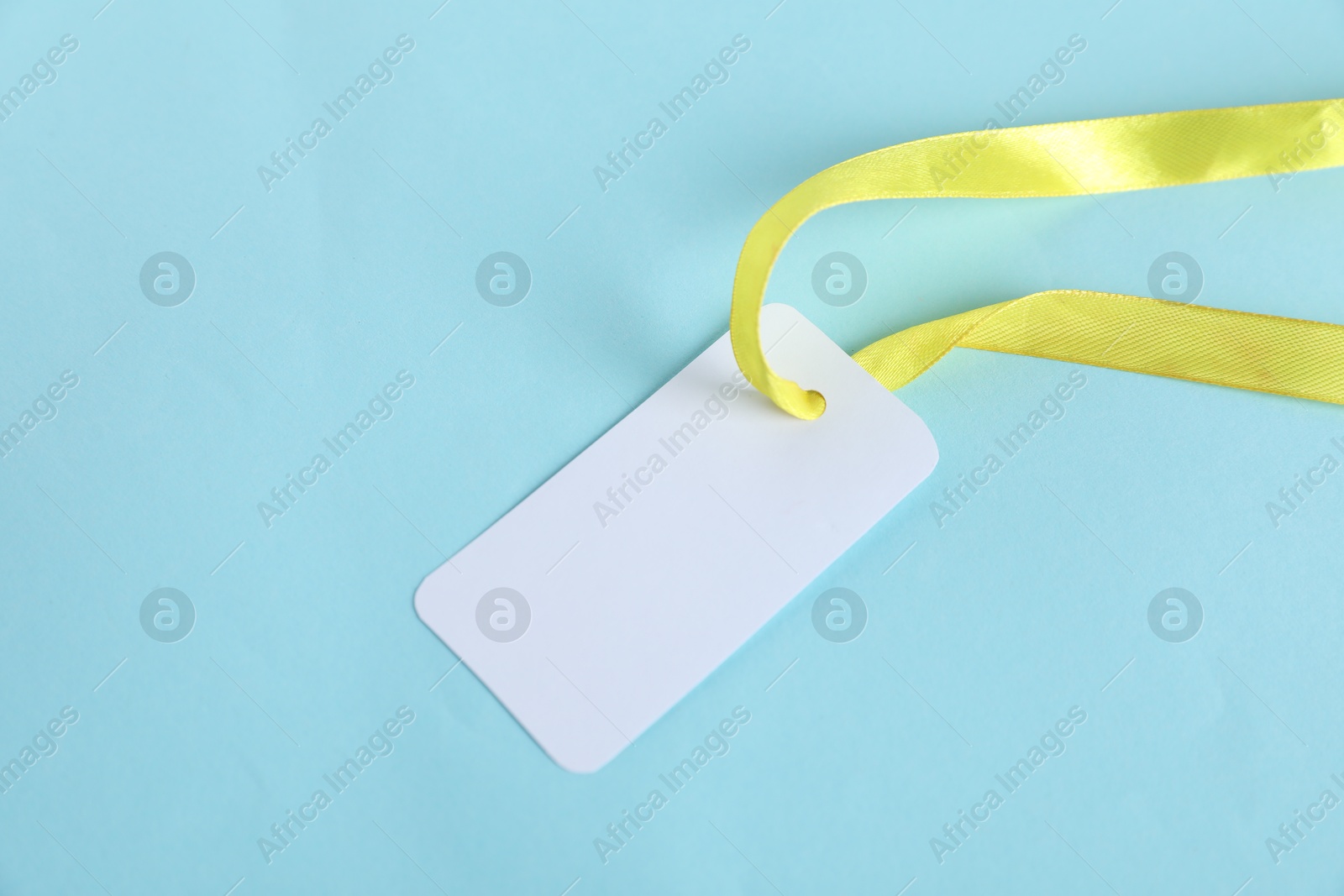 Photo of Blank tag with ribbon on light blue background, top view