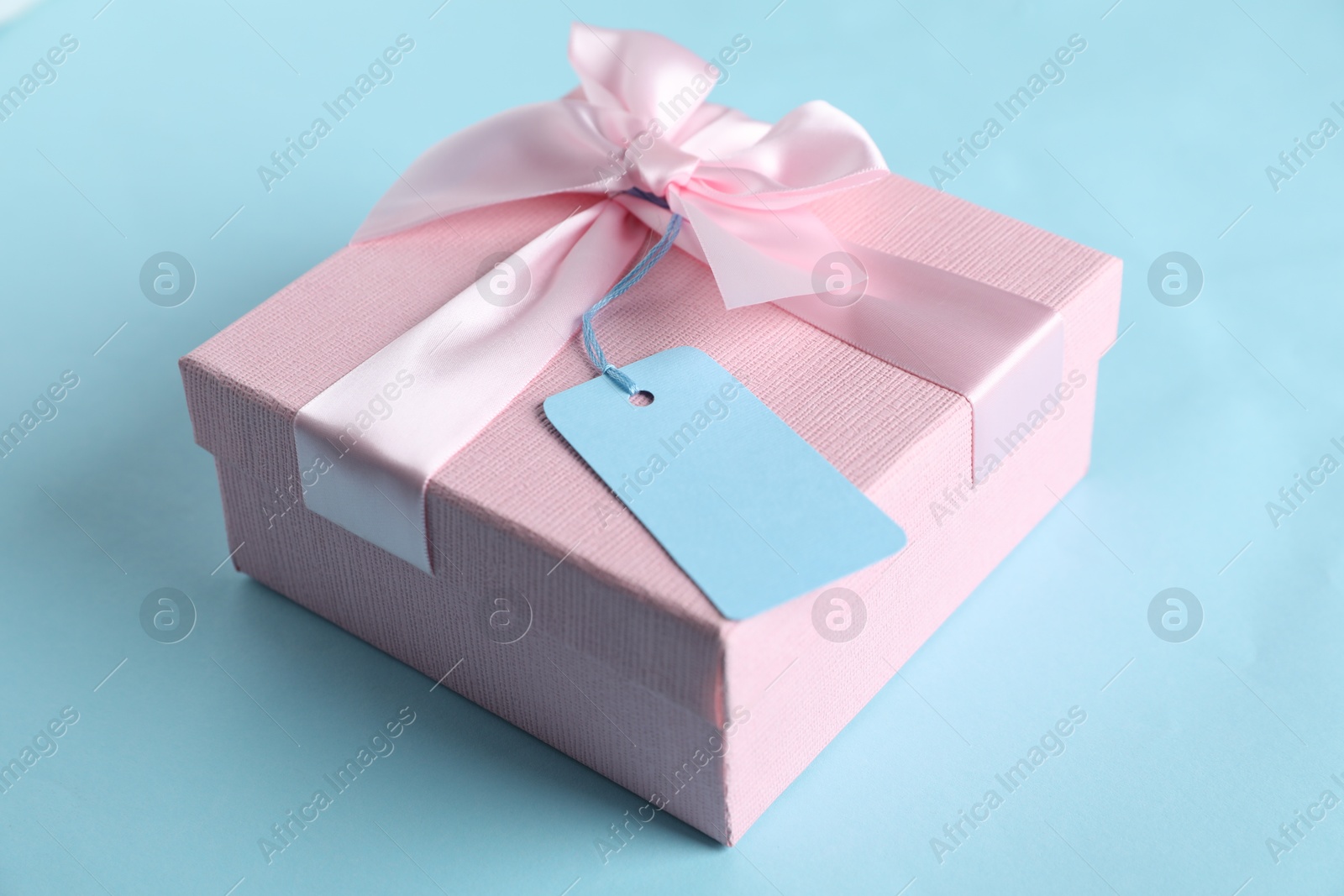 Photo of Gift box with blank tag on light blue background, closeup