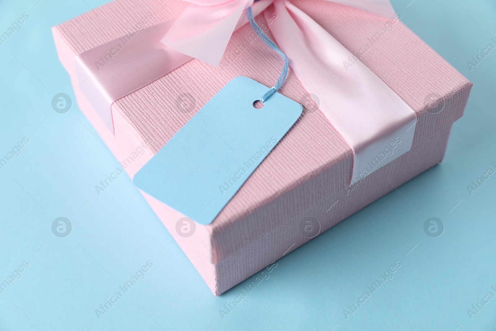 Photo of Gift box with blank tag on light blue background, closeup