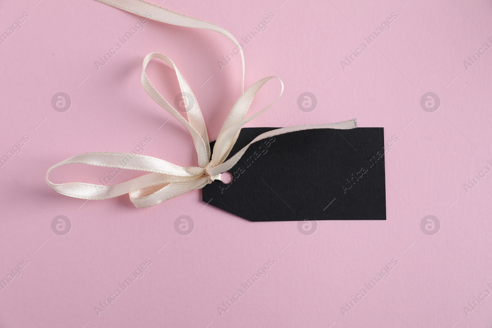 Photo of Blank tag with ribbon on light pink background, top view