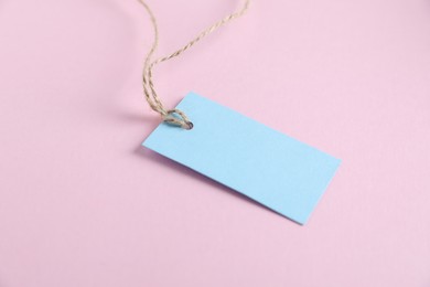 Photo of Blank tag with string on light pink background, closeup