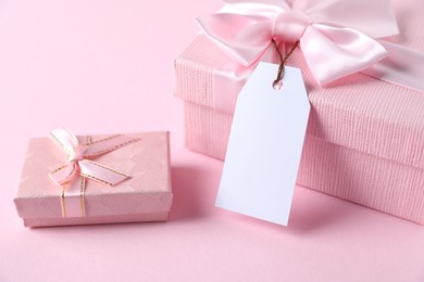 Photo of Gift boxes with blank tag on light pink background, closeup