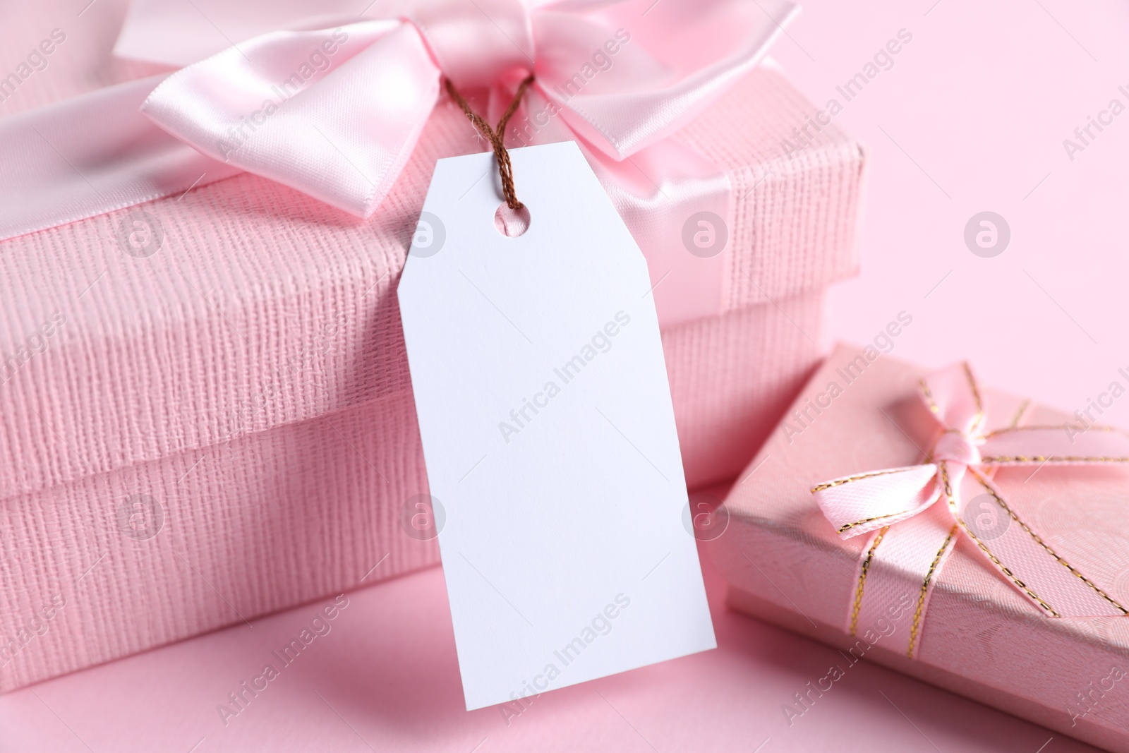 Photo of Gift boxes with blank tag on light pink background, closeup