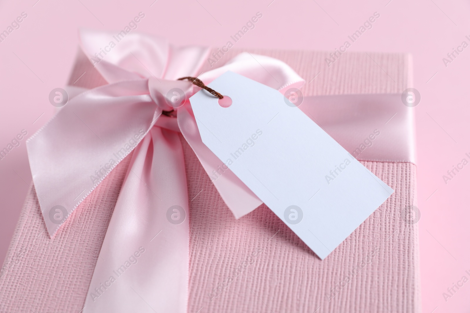 Photo of Gift box with blank tag on light pink background, closeup