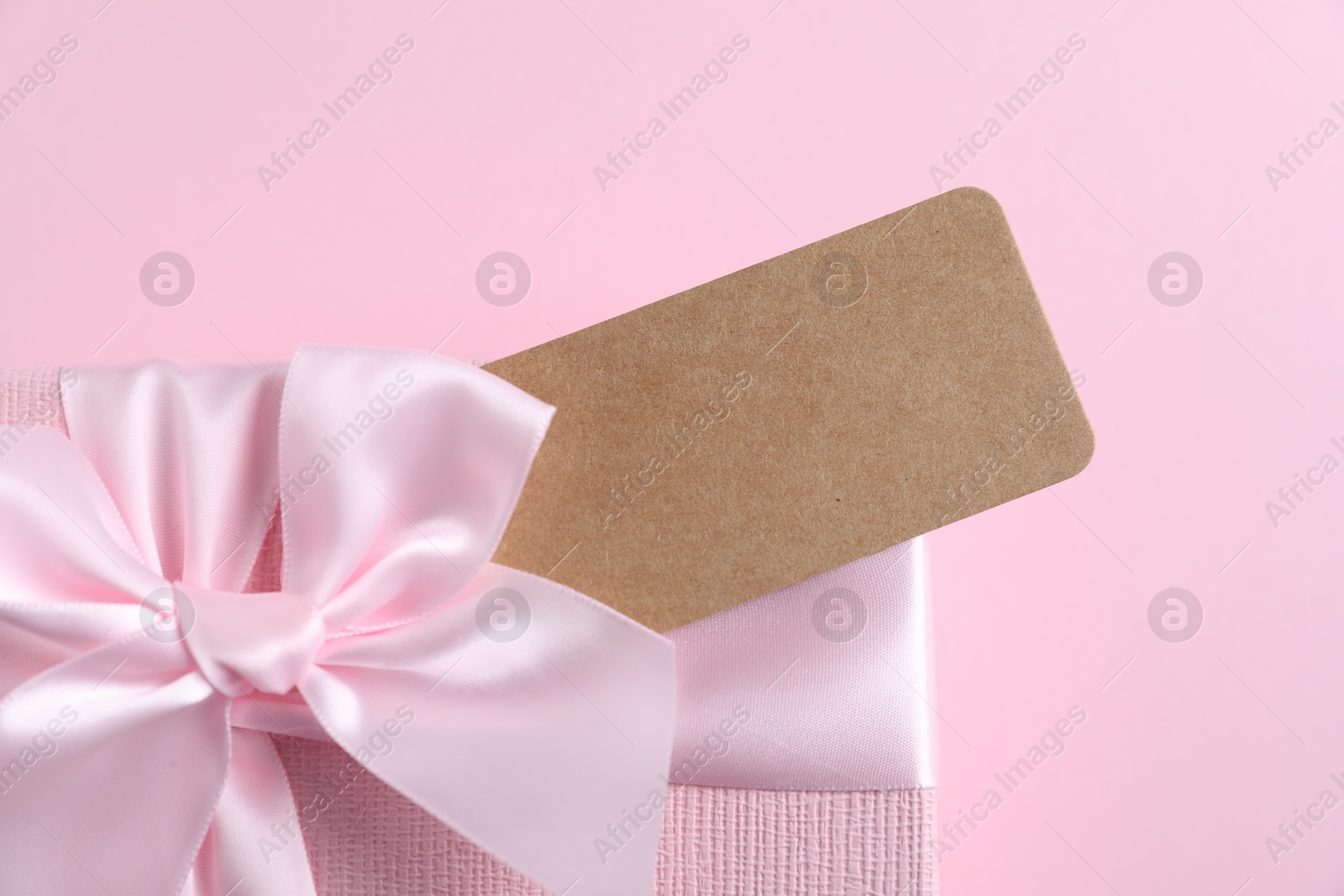 Photo of Gift box with blank tag on light pink background, closeup